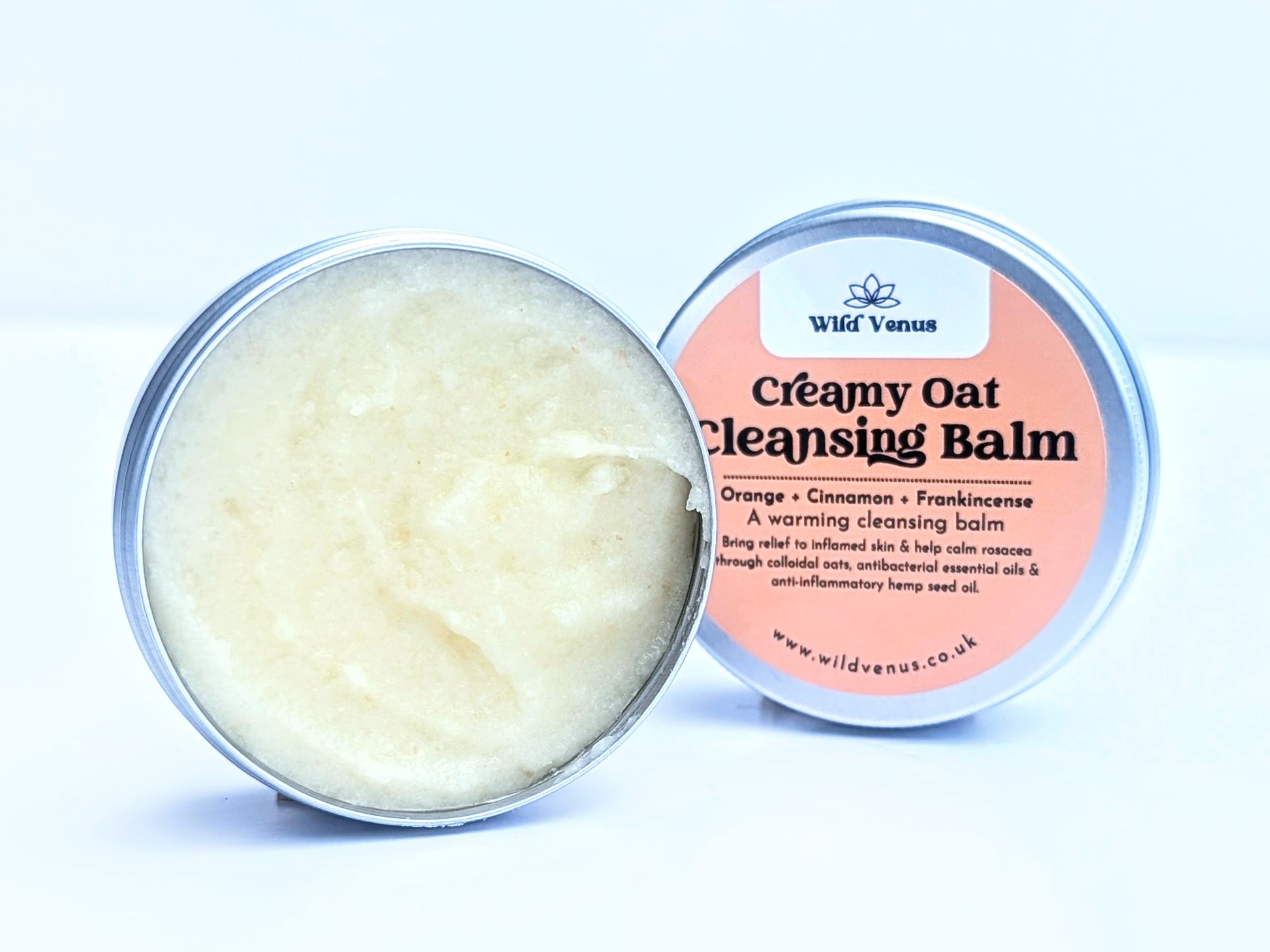 A tin of Creamy Oat Cleansing Balm with lid tucked behind the open tin. 