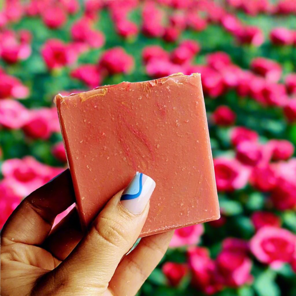 Holding a bar of damson roses bar of soap against a background of roses.