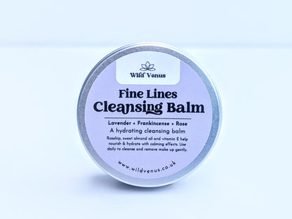 A tin of Fine Lines Cleansing Balm. This tin is on its side and front on so you can see the whole label on the tin lid. The product is shot against a plain white background. 