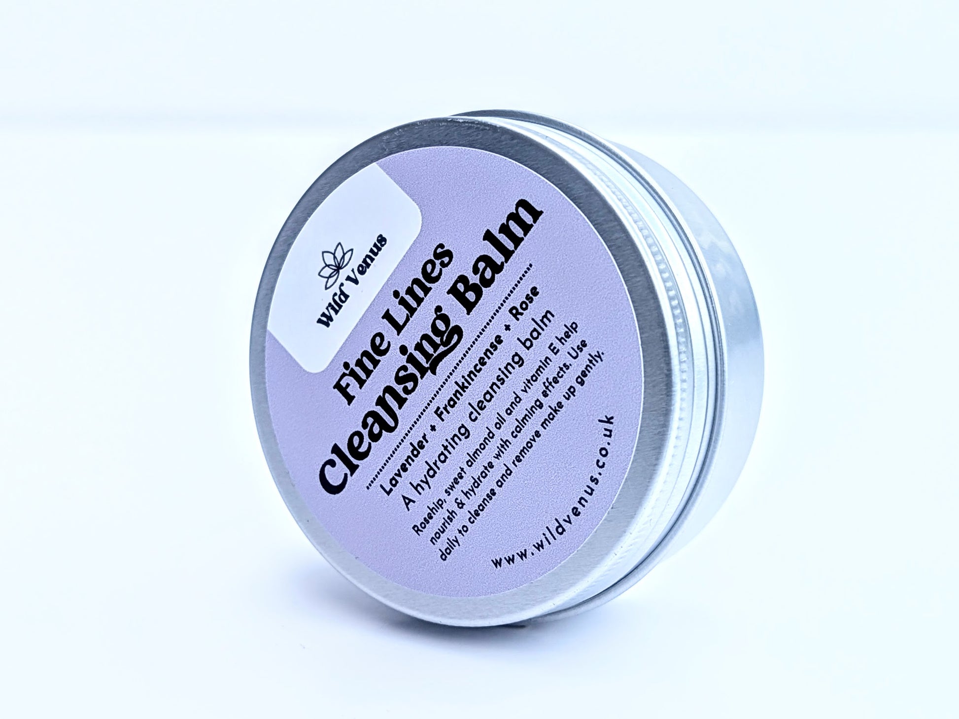 A tin of Fine Lines Cleansing Balm. This tin is on its side and tilted to the side on so you can see the whole label on the tin lid. The product is shot against a plain white background. 
