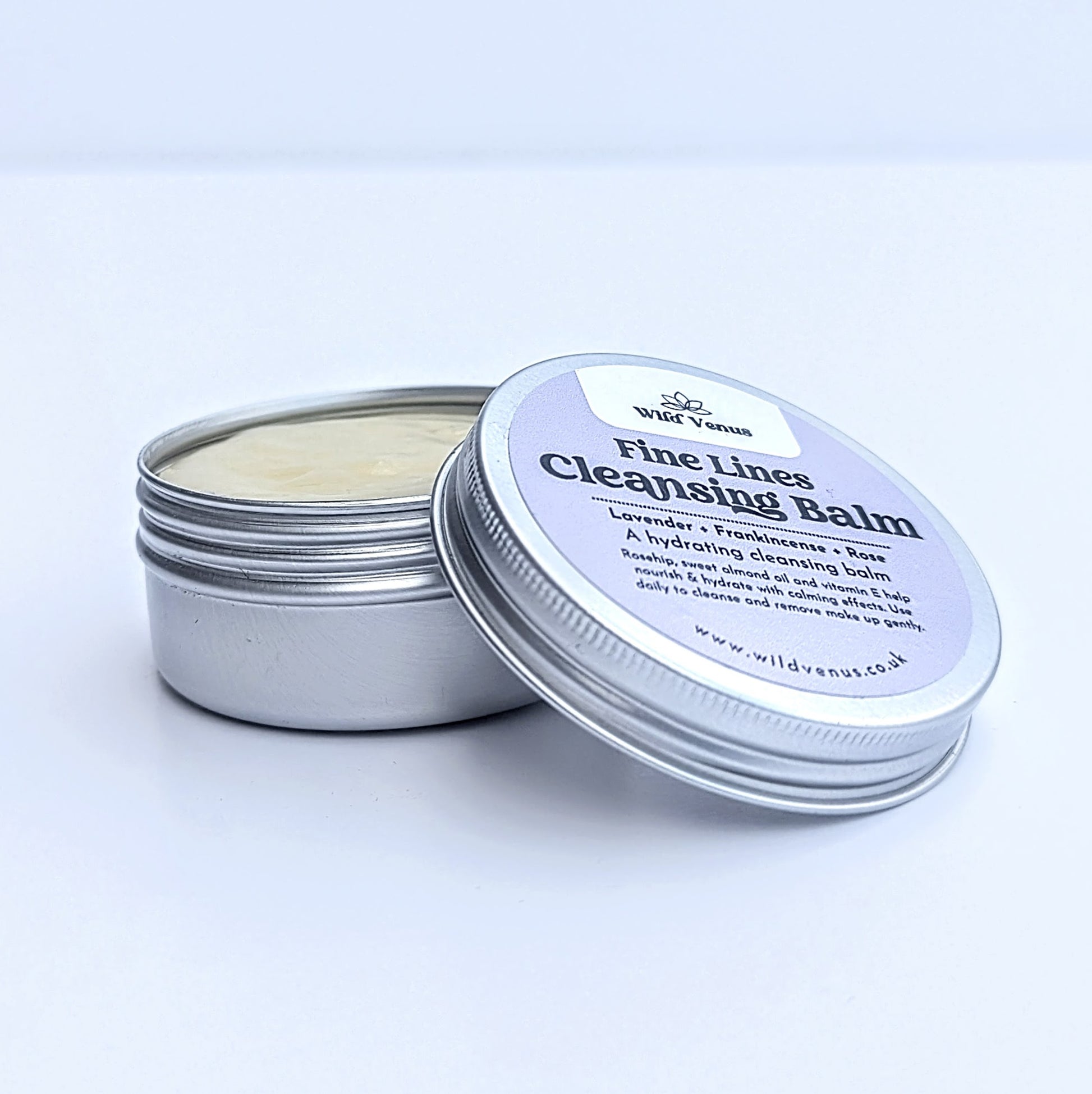 A tin of Fine Lines Cleansing Balm. The tin is open and the lid is resting against the side of the open tin. The product is shot against a plain white background. 