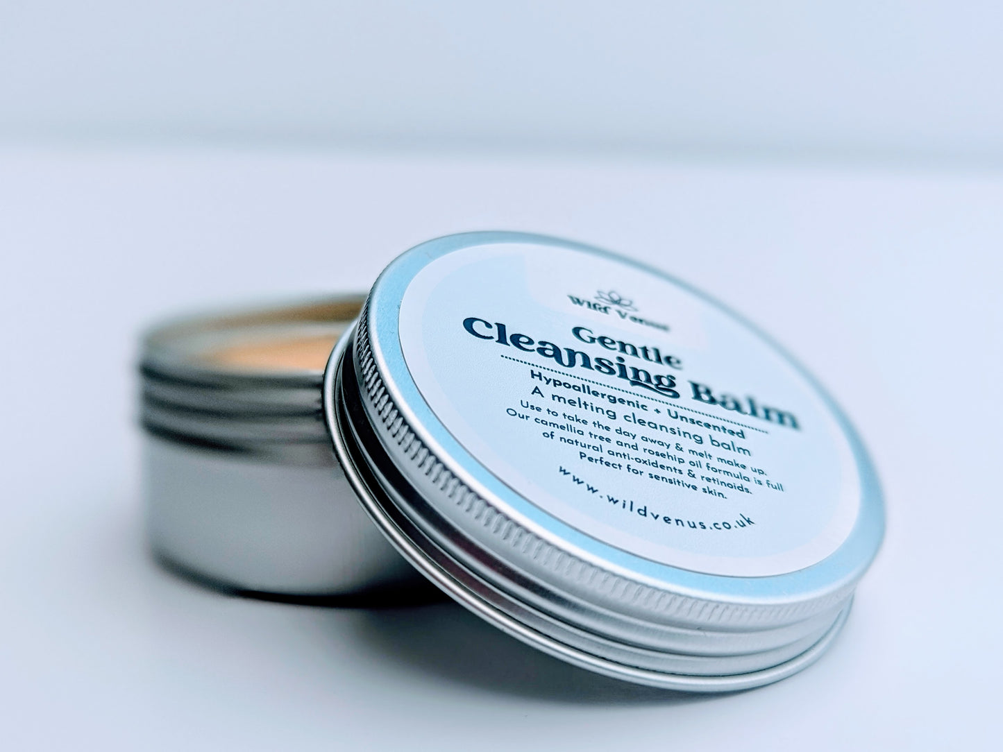 A tin of Gentle Cleansing Balm with the lid off. The tin lid is resting against the open pot. The product is against a plain white background. 