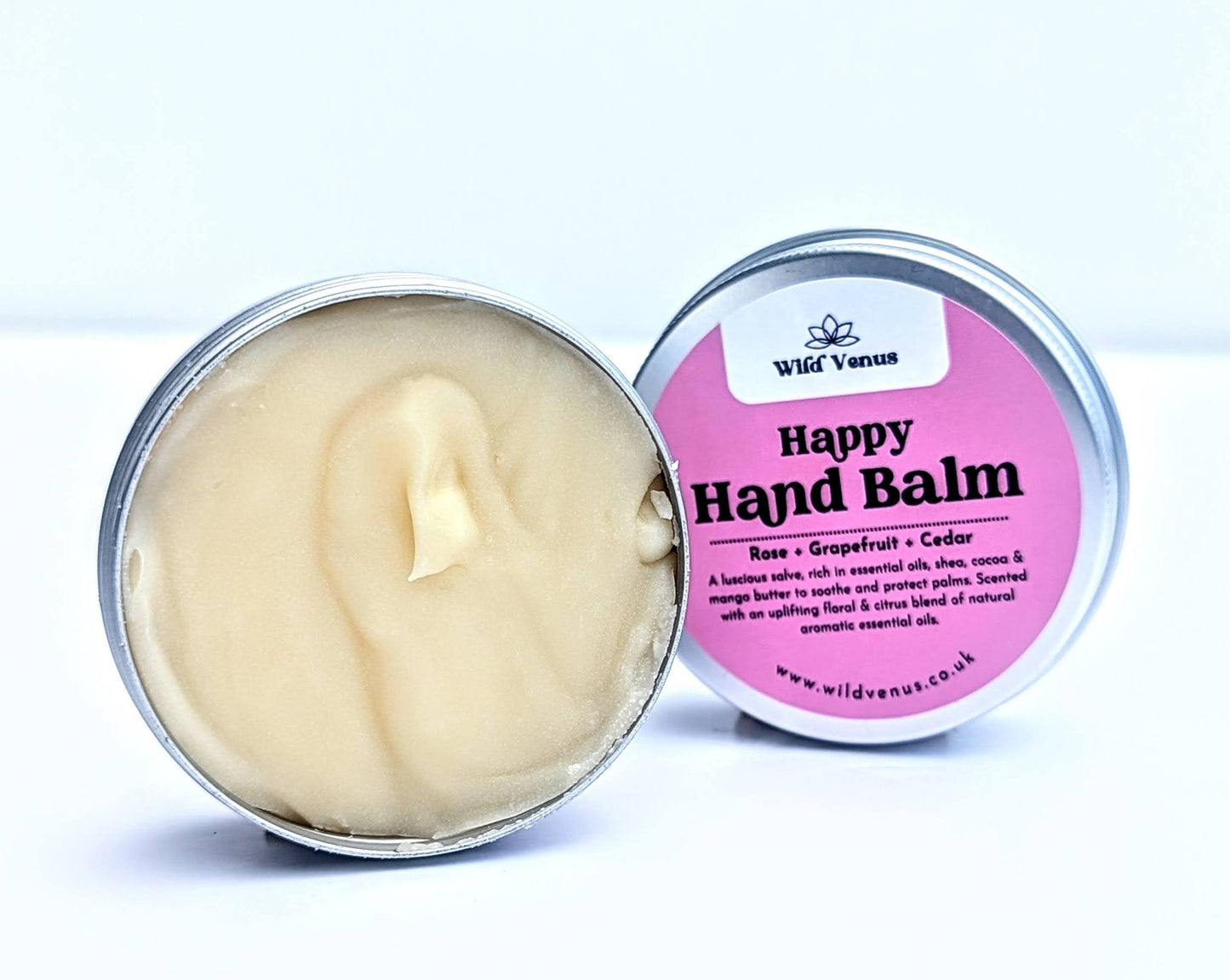 An open tin of Happy Hand Balm on a white surface against a white background. 