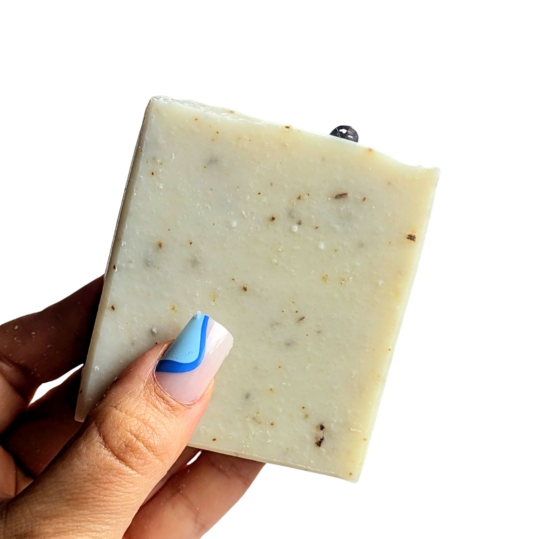 Holding a naked bar of herb garden soap against a white background. 