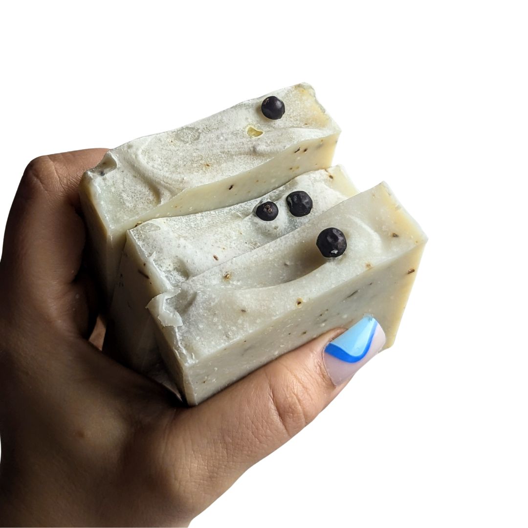 A hand holds a stack of 3 soaps against a white background. 