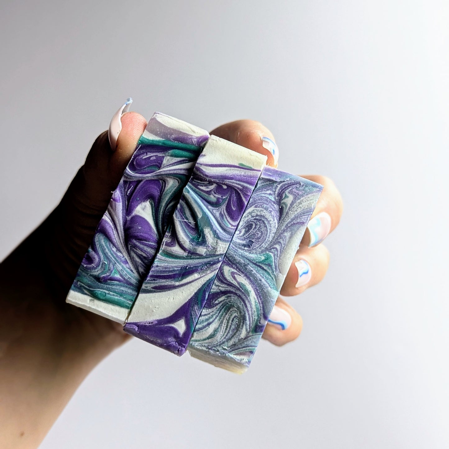 Holding 3 lavender and tea tree soaps together in one hand, pointing the swirly colourful tops towards you.