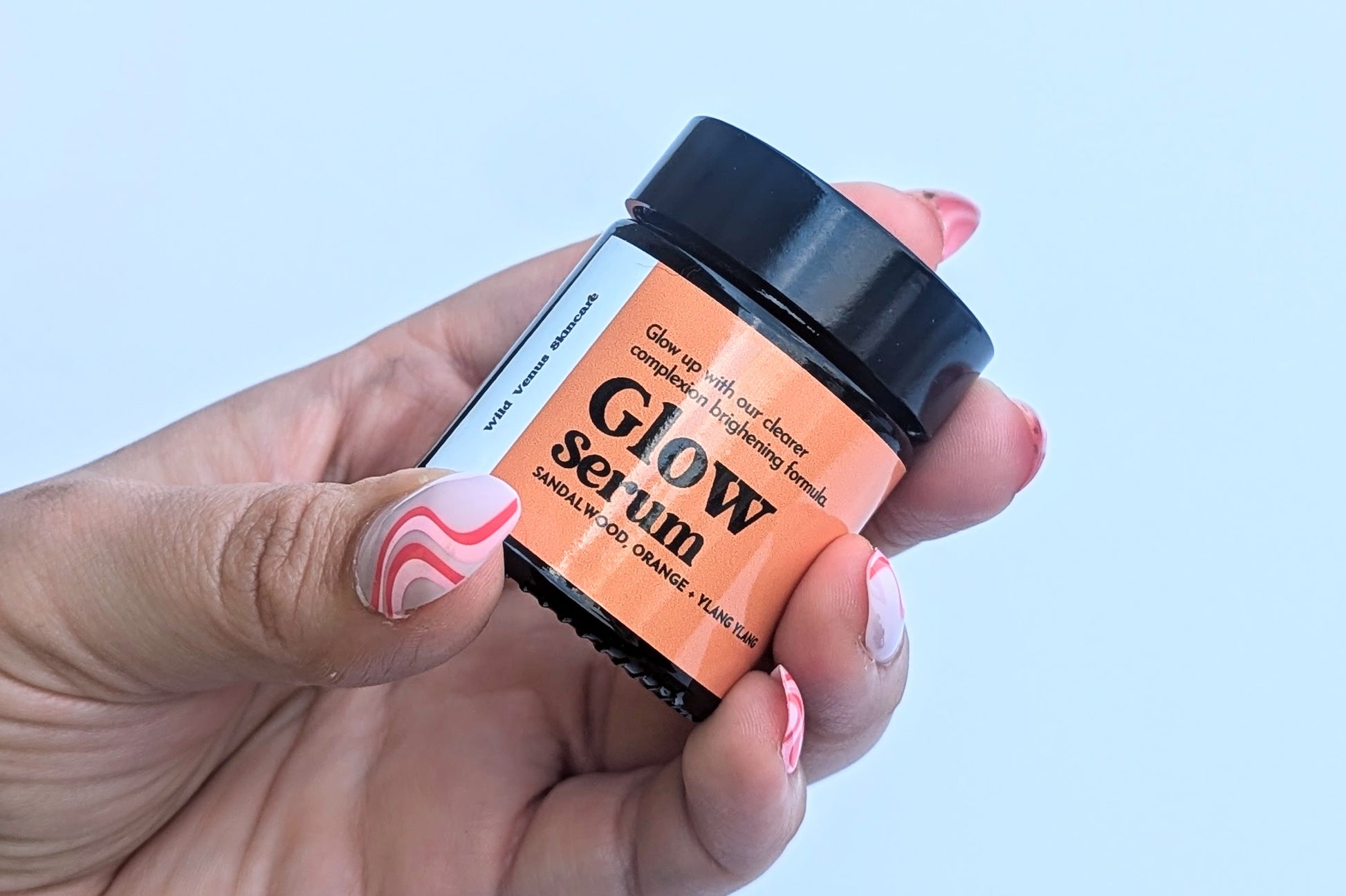 A ladies hand holds a pot of the Glow serum up against a white background. 