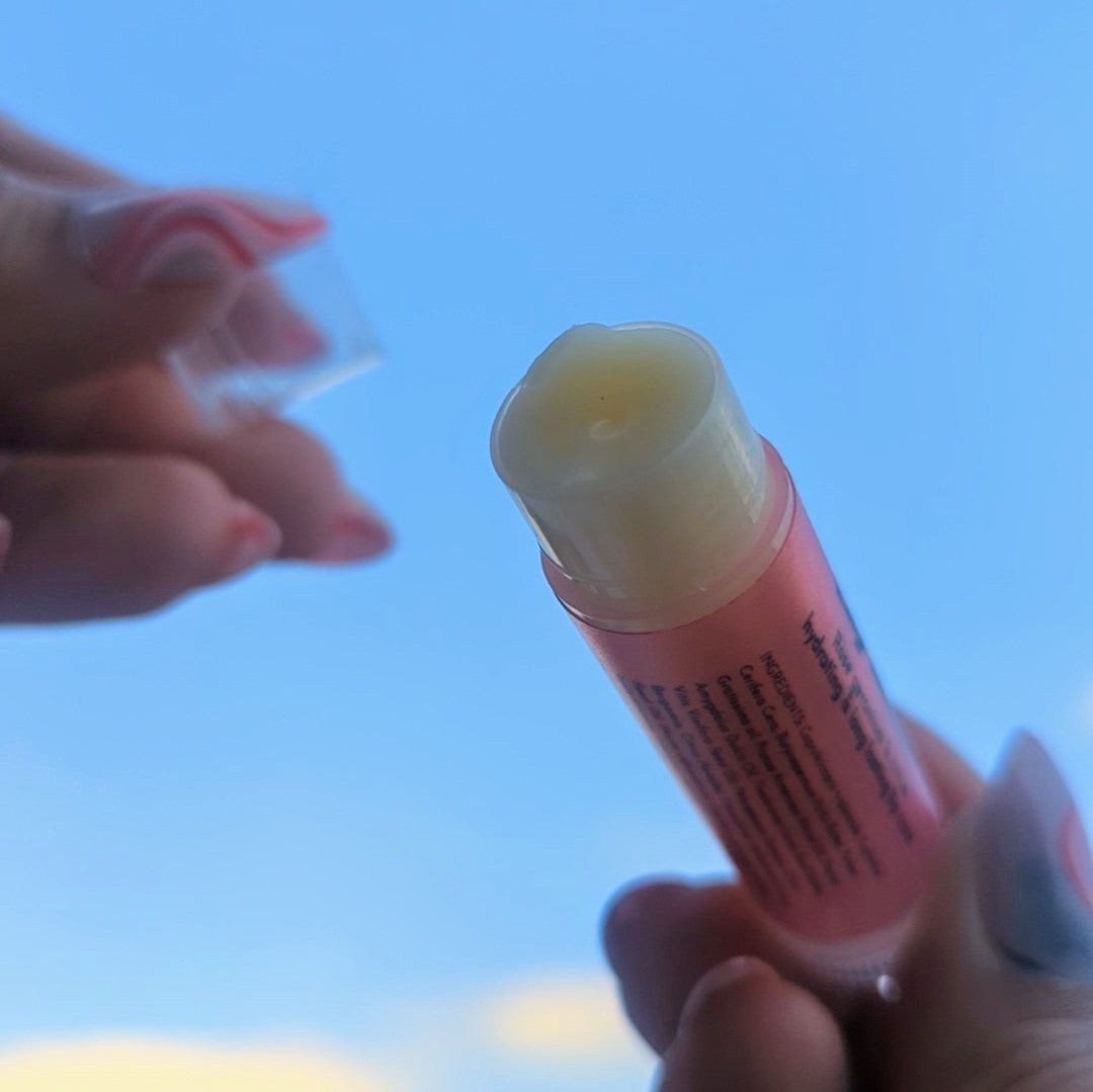 Holding a n open strawberry lip balm up to the sky.