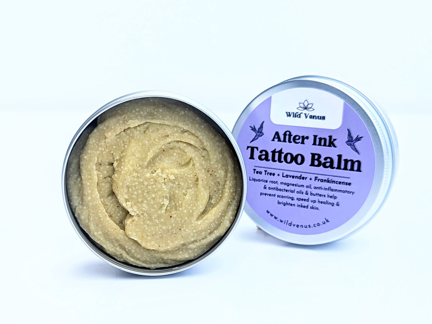 An open tin of the After Ink tattoo balm against a white background. The tin lid is tucked behind the balm. The balm shows a deep rich colour and texture. 