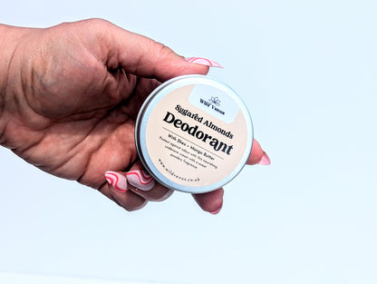 A hand with funky pale pink nails hold a tin of Sugared Almonds Deodorant towards the camera against a white background. 