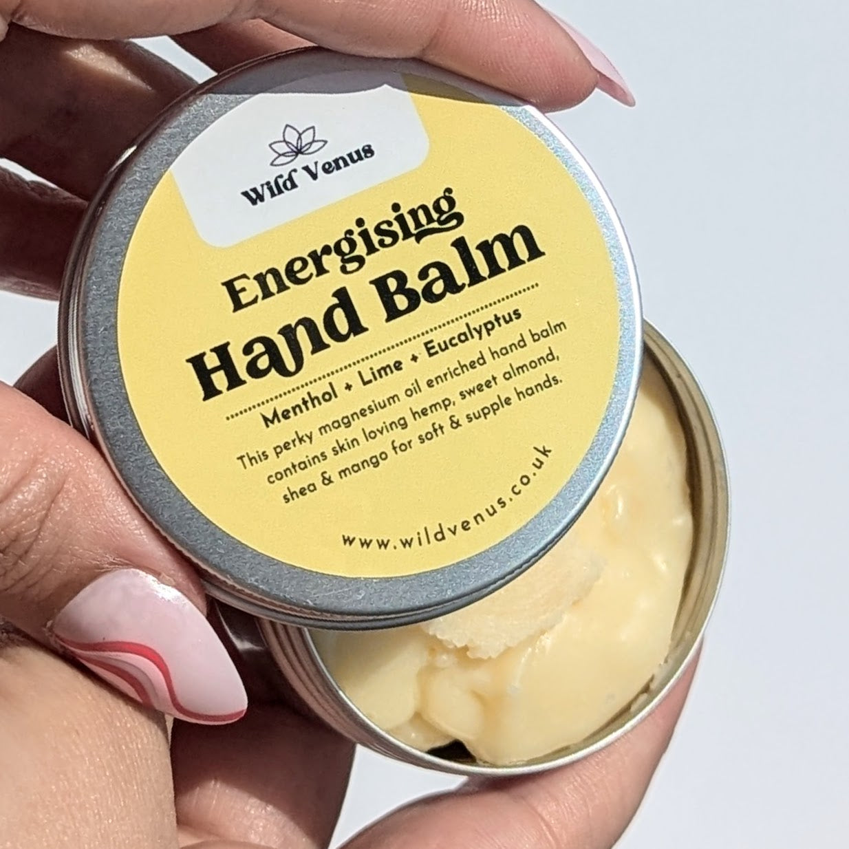 Holding an open tin of energising hand balm. 